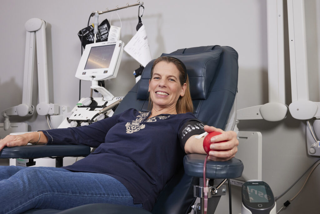 Smiling blood donor with squeezing a red foam heart as she donates.