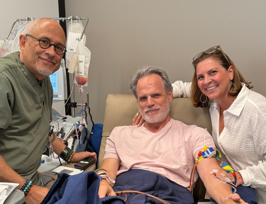 Actor Michael Park donating blood with his wife Laurie Nowak and a Comprehensive Cell Solutions representative next to him, at New York Blood Center Rye Donor Center.