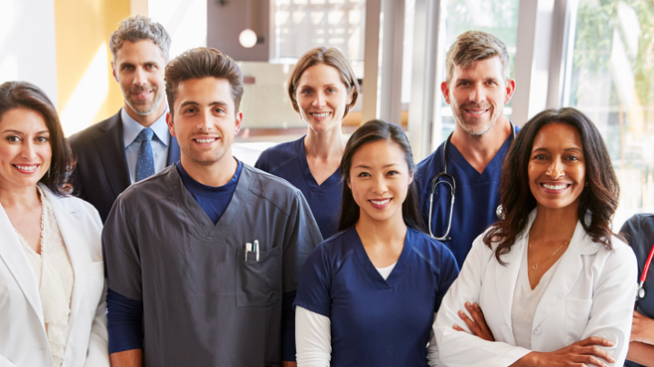 Diverse group of nine smiling Community Blood Center staff featuring phlebotomists, laboratory and office staff.